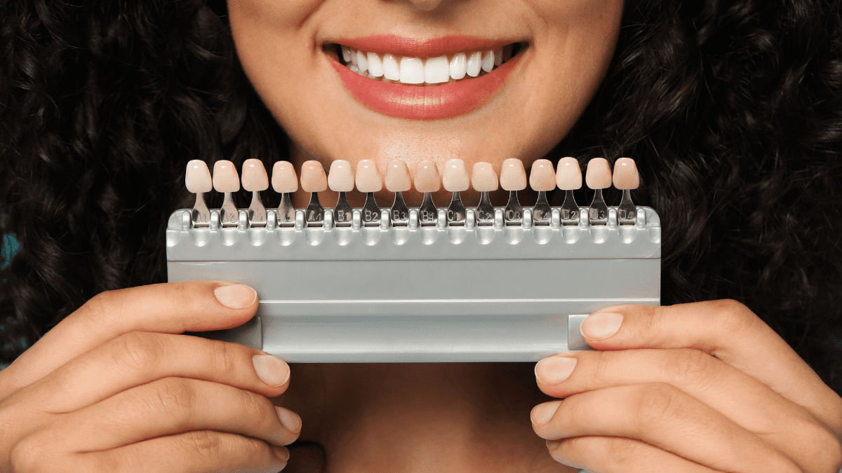 Woman smiling and holding a shade guide for porcelain veneers.